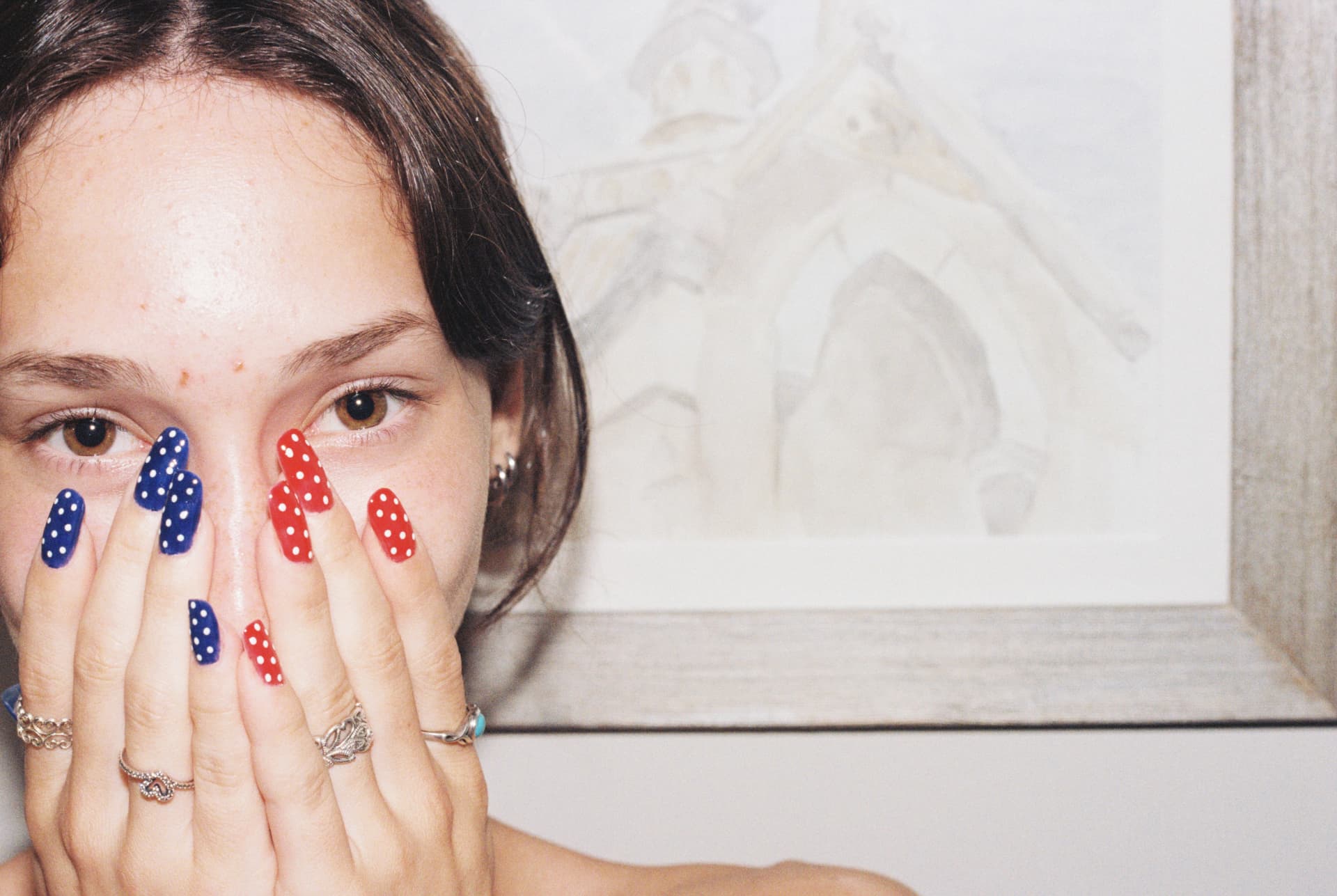 Close-up portrait with red and blue patterned fingernails held over the face