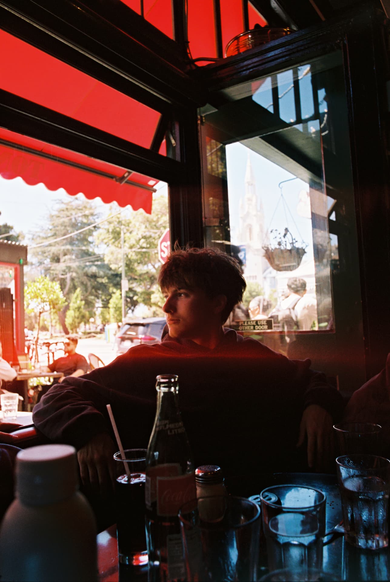 Person seated at a cafe table beneath a red awning