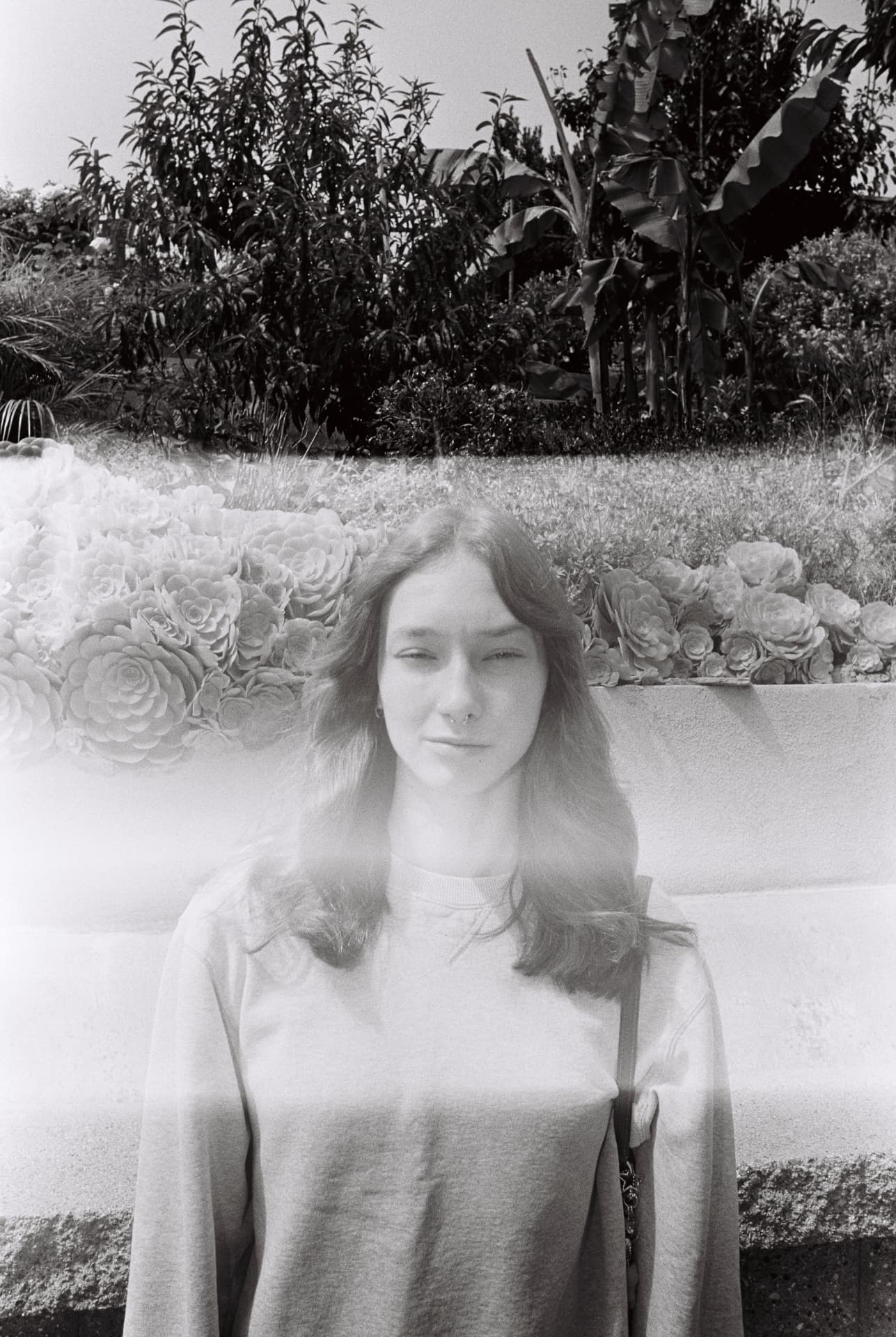 Black-and-white double exposure of a woman and garden foliage